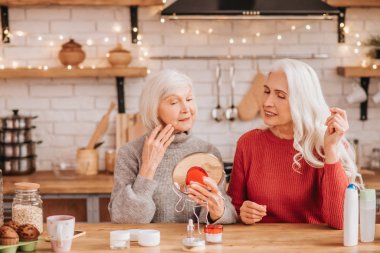 Two good-looking elderly women trying new cream