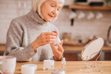 Grey-haired beautiful lady in grey blouse opening a jar of cream