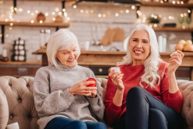 Two grey-haired pleasant cute ladies discusing new anti-aging creams