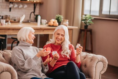 Two grey-haired pleasant cute ladies talking about new anti-aging creams