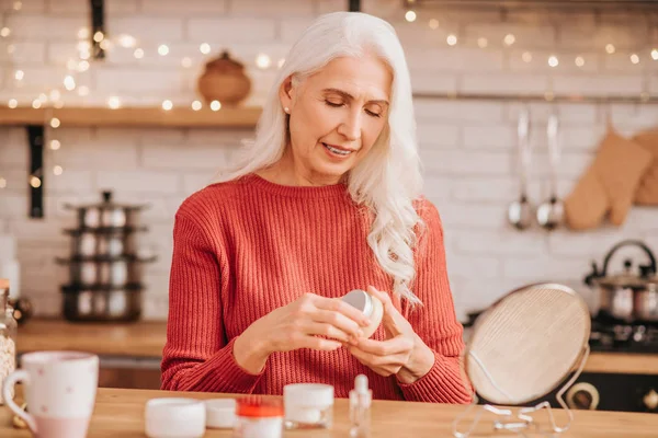 Grey-haired beautiful lady in red opening a jar of new cream