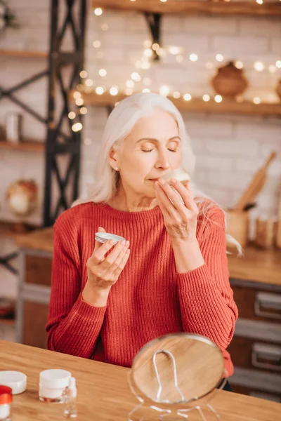 Mujer hermosa de pelo gris en rojo disfrutando de la nueva crema — Foto de Stock
