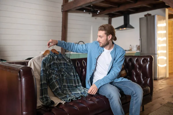 Homem colocando suas camisas no sofá — Fotografia de Stock