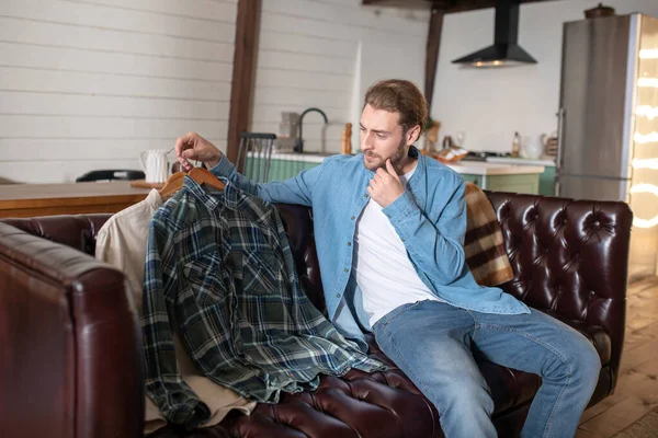 Man choosing a shirt while sitting on the sofa — Stockfoto