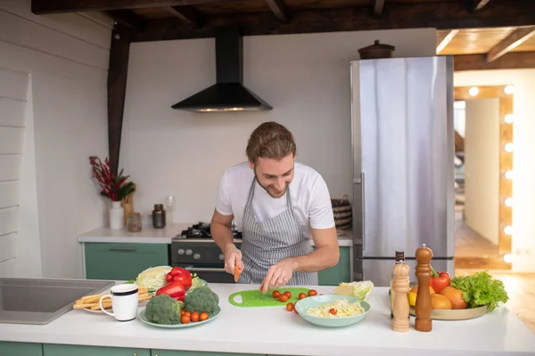 Glimlachende man die tomaten snijdt voor een salade — Stockfoto