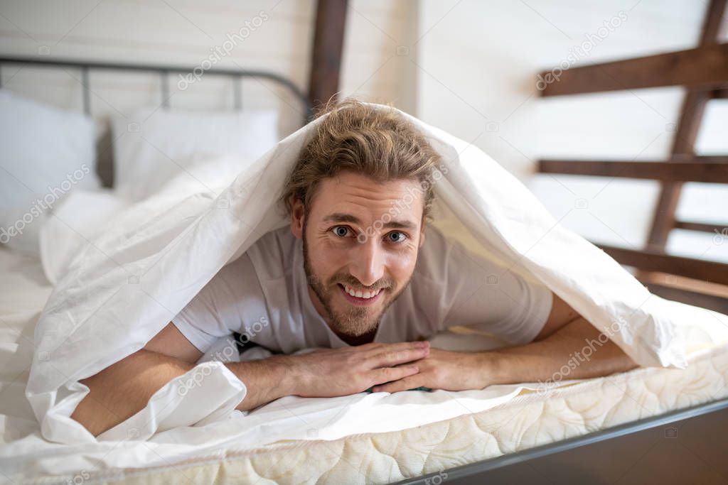 Smiling man covering himself with a blanket