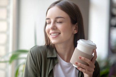 Gülümseyen kadın sabah kahvesini içerken zevk alıyor.