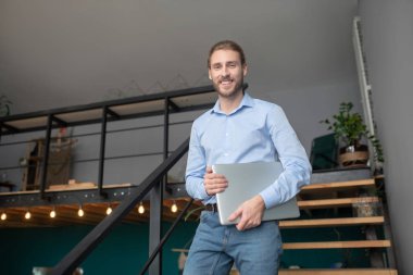 Gömlek giyen yakışıklı adam bilgisayarını tutuyor.