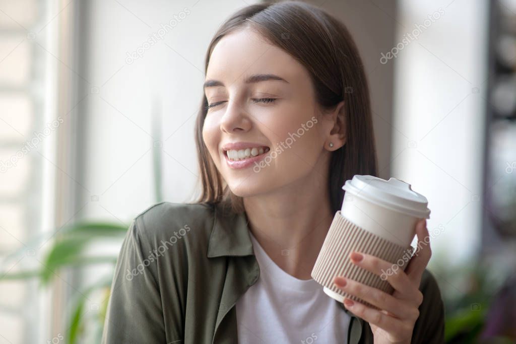 Smiling woman having a pleasure while drinking morning coffee