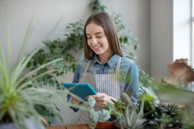Önlük takan gülümseyen kadın bitkilerle ilgileniyor.