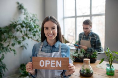 Önlüklü gülümseyen kadın ilk müşteriye hoş geldin diyor.