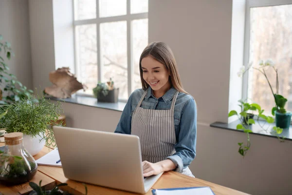 Ung kvinna bär ett förkläde som arbetar med en dator — Stockfoto