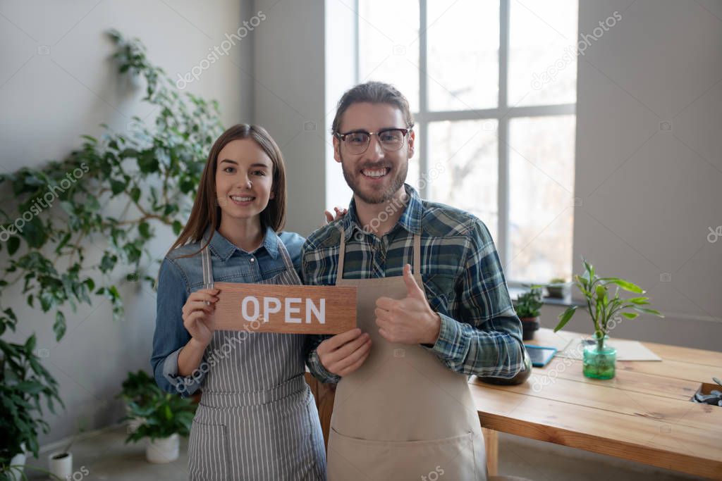 Smiling man and woman holding the open sign