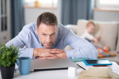 Mavi gömlekli sakallı adam düşünceli görünüyor.