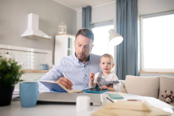 Skäggig man i blå skjorta håller sitt barn och ser koncentrerad ut — Stockfoto