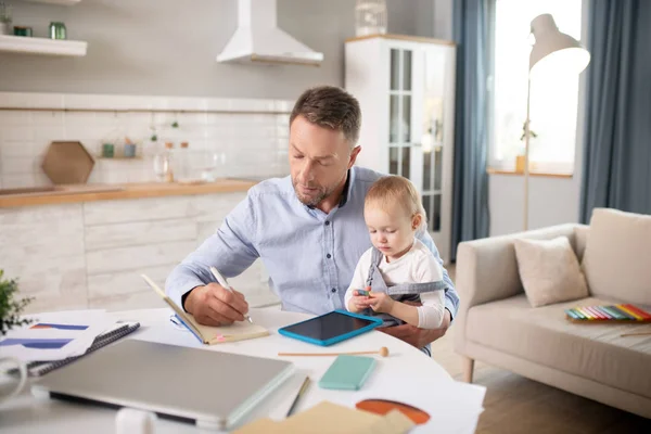 Bearded man in a blue shirt holding his kid and looking serious — Stock Photo, Image