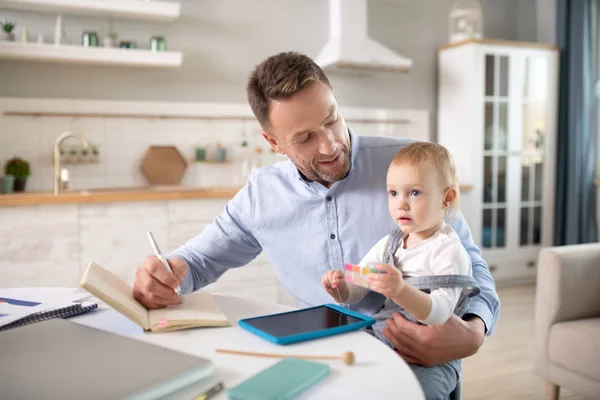 Homem barbudo com uma camisa azul segurando seu filho e fazendo anotações — Fotografia de Stock