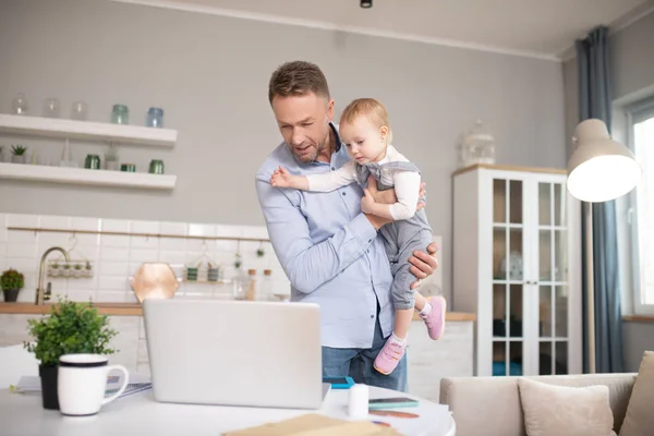 Man in een blauw shirt staand en kijkend naar de laptop — Stockfoto