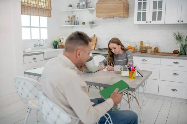 Hombre barbudo de pelo corto mirando el libro verde en sus manos — Foto de Stock