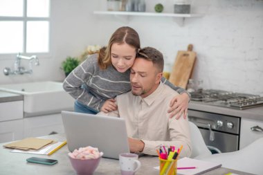 Gri gömlekli uzun saçlı kız babasına sarılıyor.