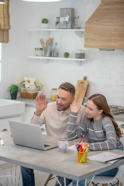 Långhårig flicka i grå skjorta och hennes far pratar online med vänner — Stockfoto