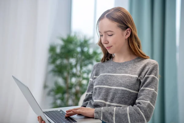 Długowłosy dziewczyna w szarej koszuli trzyma laptopa — Zdjęcie stockowe