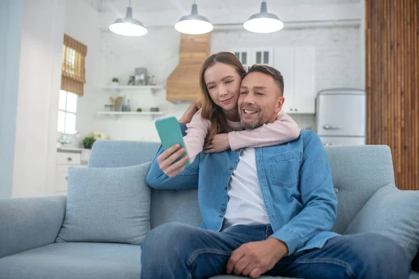 Daughter photographing herself with her father on smartphone. — Stock Photo, Image