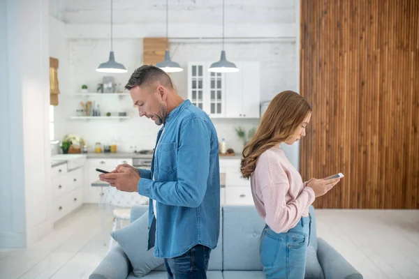 Padre e hija de pie espalda con espalda mirando sus teléfonos inteligentes . —  Fotos de Stock