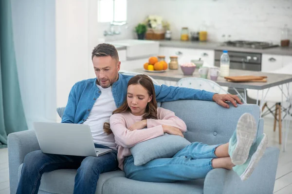 Dad and daughter looking at laptop screen sitting on sofa. — Stock Photo, Image