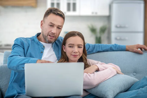 Father pointing to laptop screen and daughter sitting on couch. — Stock Photo, Image