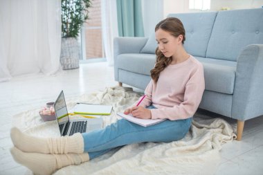 Kanepenin yanındaki yerde oturan kız..