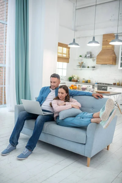 Daughter with father looking at laptop on sofa at home. — Stock Photo, Image