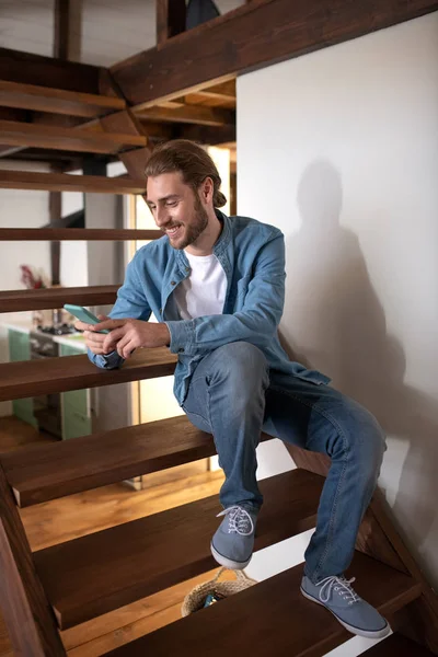 Smiling man texting with friend while sitting on the stairs — Stok Foto