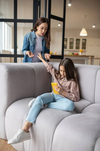 Hija traviesa con smartphone en la mano sentada en el sofá . — Foto de Stock