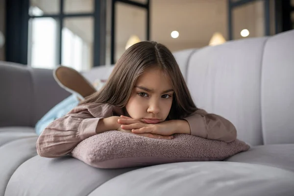 Klein meisje met een droevige blik liggend op de bank. — Stockfoto