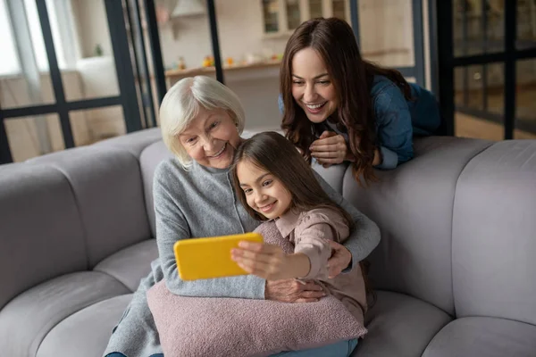 Chica feliz, mamá, abuela tomando fotos juntos en casa en el sofá . — Foto de Stock