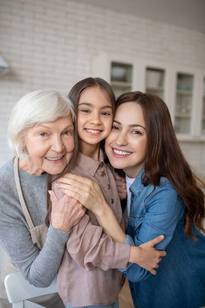 Three happy women hugging together in the kitchen. — Stock Photo, Image