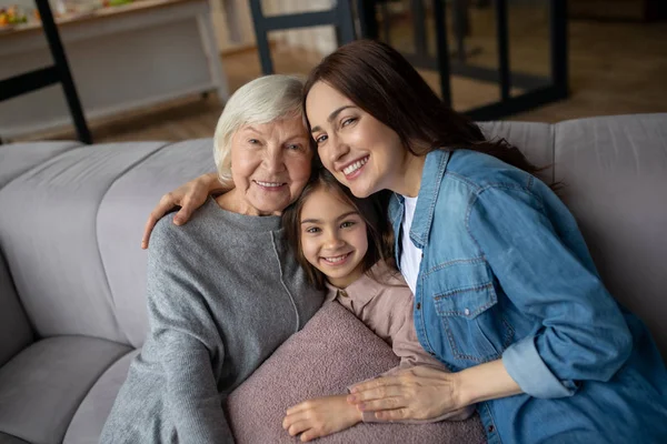 Girl, mom, grandmother sitting hugging on the couch. — Stock Photo, Image