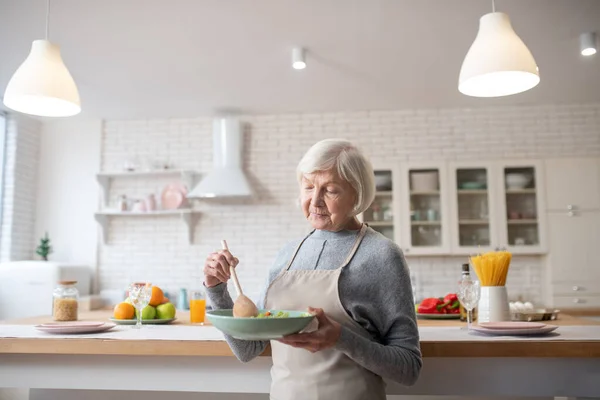 Nonna in piedi in cucina con un'insalata di verdure . — Foto Stock