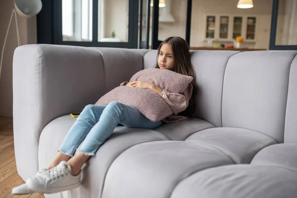 Gadis kecil yang sedih duduk di sofa di rumah . — Stok Foto