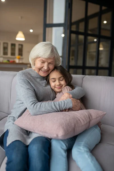 Grandmother hugging tightly granddaughter sitting on the couch.