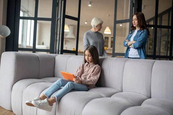 Petite fille avec tablette dans les mains assise sur le canapé . — Photo