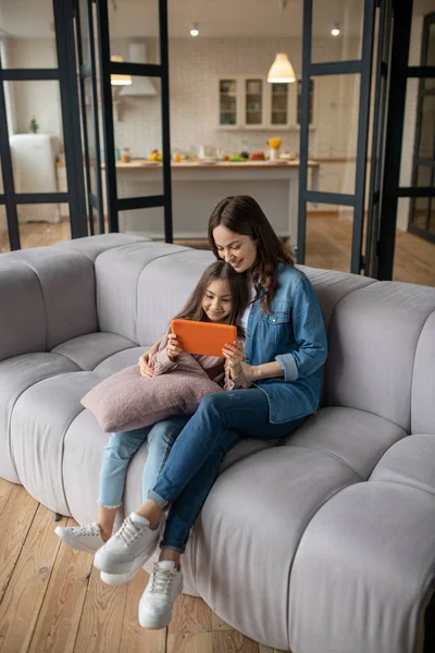 Hija con la tableta en las manos y mamá sentada en el sofá . — Foto de Stock