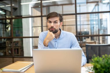 Mavi gömlekli sakallı adam düşünceli görünüyor.