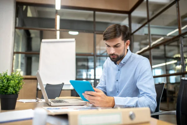 Bearded man in a blue shirt holding a tablet and looking concentrated — Stockfoto