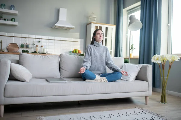 Молодая девушка в сером свитере медитирует в позе лотоса — стоковое фото