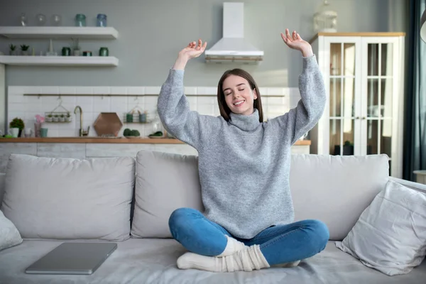 Young girl in a grey sweater sitting on the sofa and stretching — Stock Photo, Image