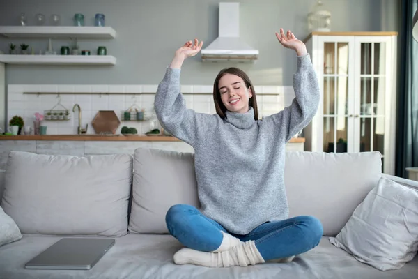 Chica joven en un suéter gris sentado en el sofá y estiramiento — Foto de Stock