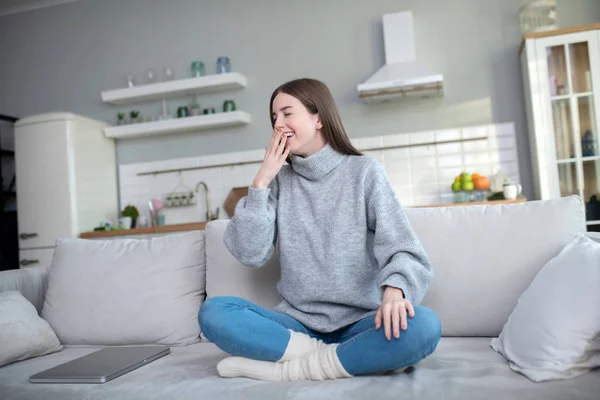 Chica joven en un suéter gris sentada en el sofá y bostezando — Foto de Stock