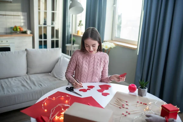 Donkerharig meisje in een roze overhemd dat hart uitsnijdt — Stockfoto